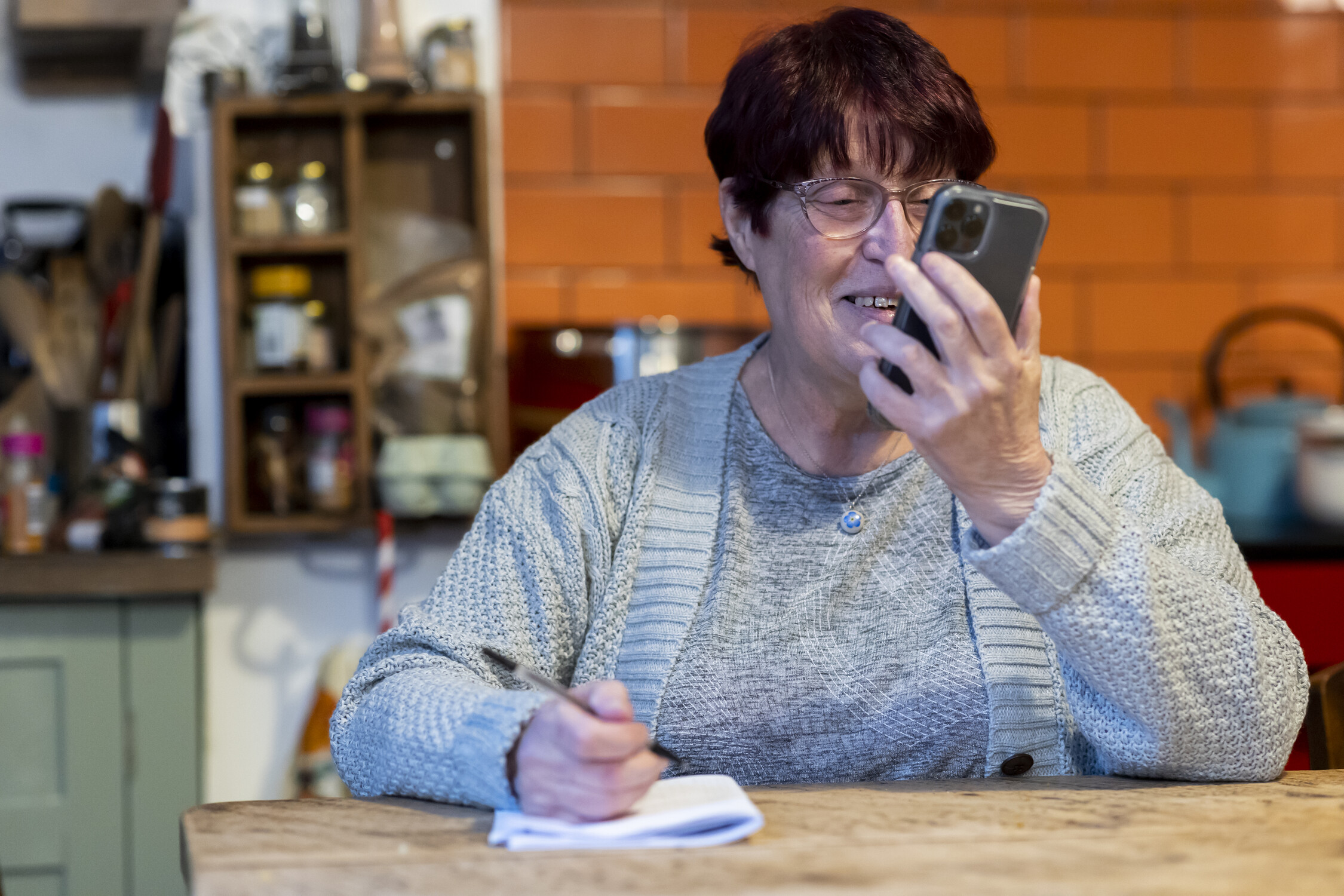 Woman is stood up on her phone noting down information on some paper.