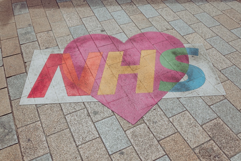 A heart-shaped sign with NHS in colorful letters is painted on a tiled pavement, symbolizing support for the UKs National Health Service.