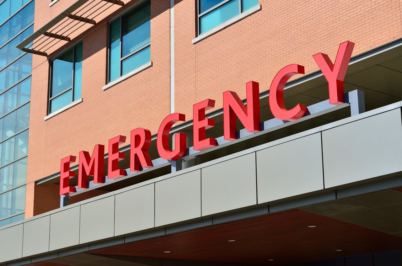 A brick building with large windows and a red sign that says 'EMERGENCY' above the entrance