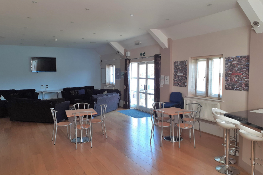 Spacious room in Romford Baptist Church with tables, chairs, sofas, a bar area, and a wall-mounted TV; large windows and decorated walls.
