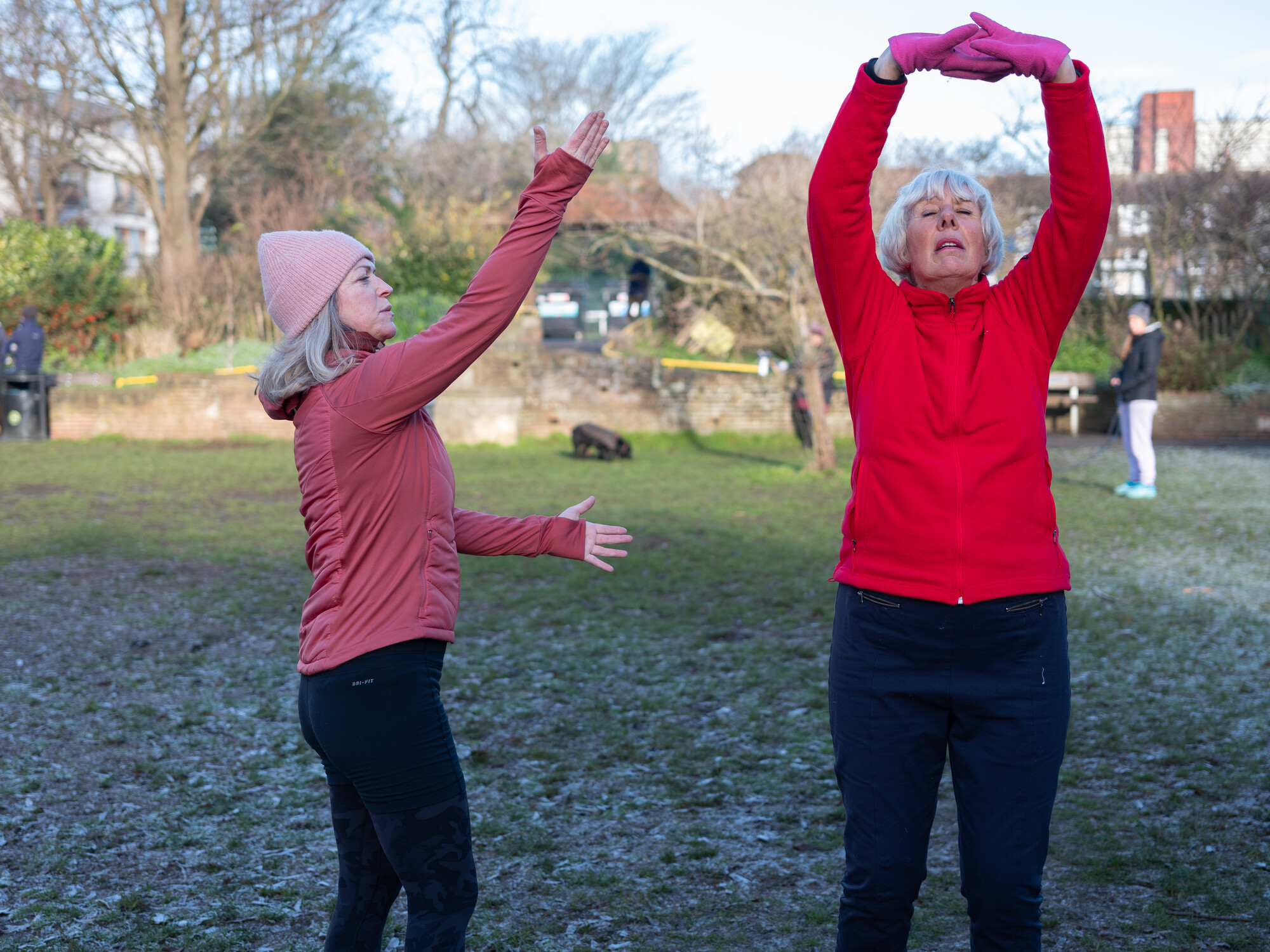 Two older women in the park at winter stretching and exercising.