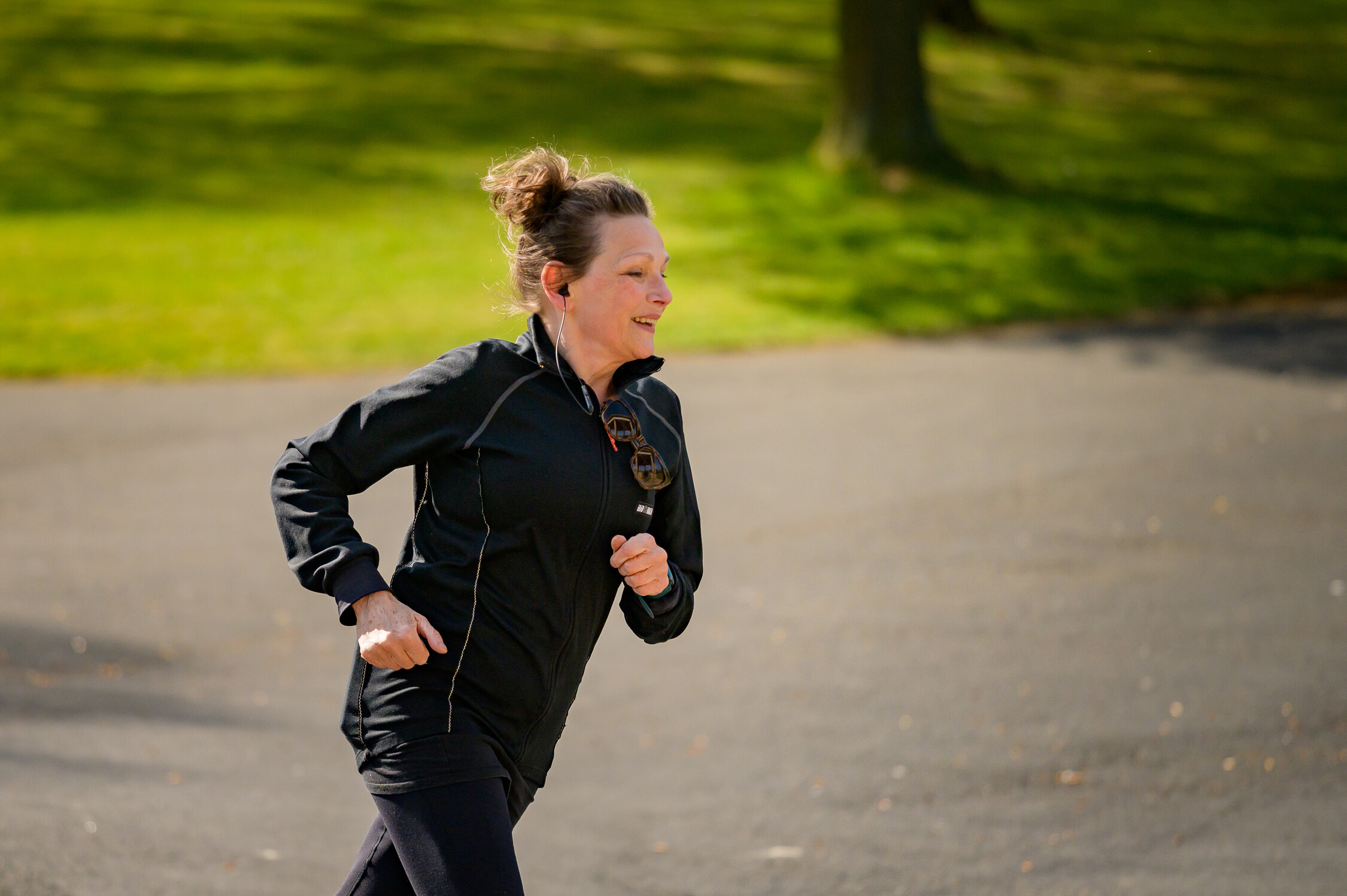 Person jogging on a paved park path, wearing a black jacket and dark leggings.