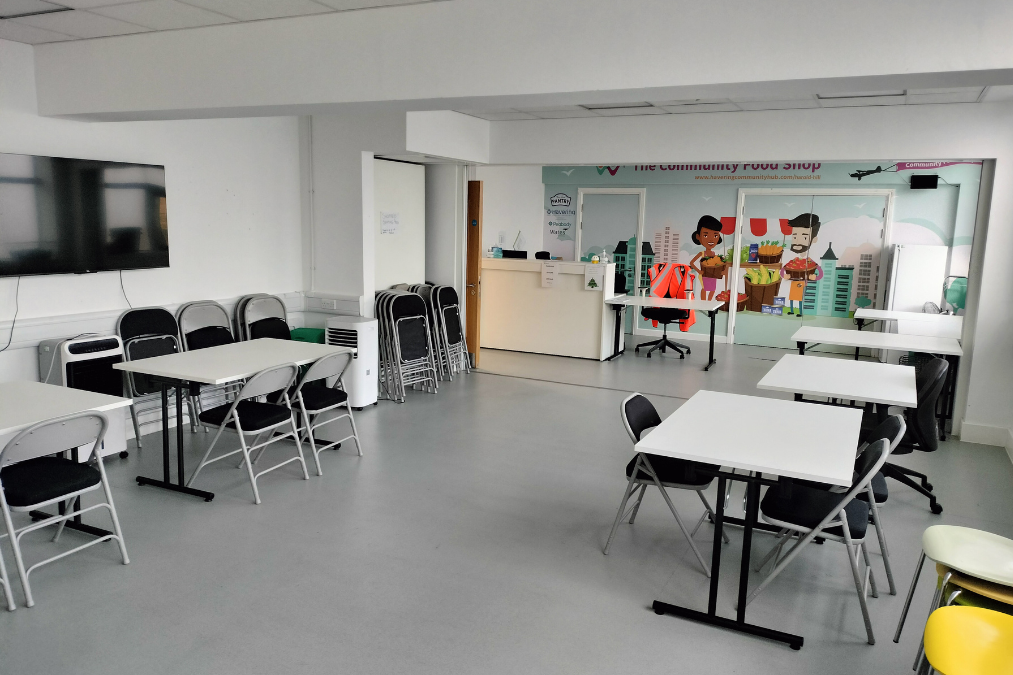 Modern room in Harold Hill library with white tables, folding chairs, a wall-mounted TV, counter area, and a colorful mural of people and buildings.