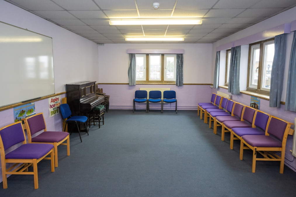 Meeting room in Romford Baptist Chuch with purple-cushioned chairs in a U-shape, upright piano, whiteboard, and posters reading “Aspire” and “hope.”