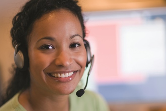 A woman is wearing a headset in a call centre and is smiling