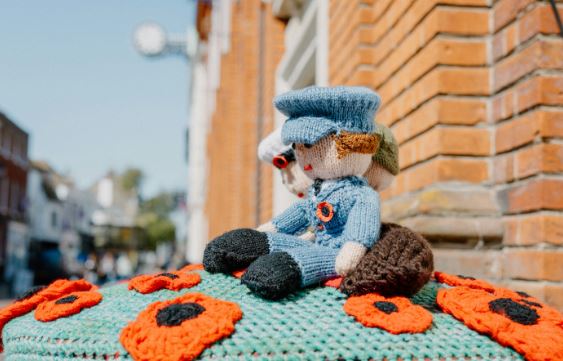 Two knitted figures in armed forces uniforms surrounded by poppies on top of a red postbox