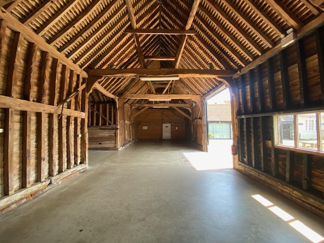 Interior of the Thames Chase barn with exposed beams, concrete floor, and sunlight streaming through an open doorway.