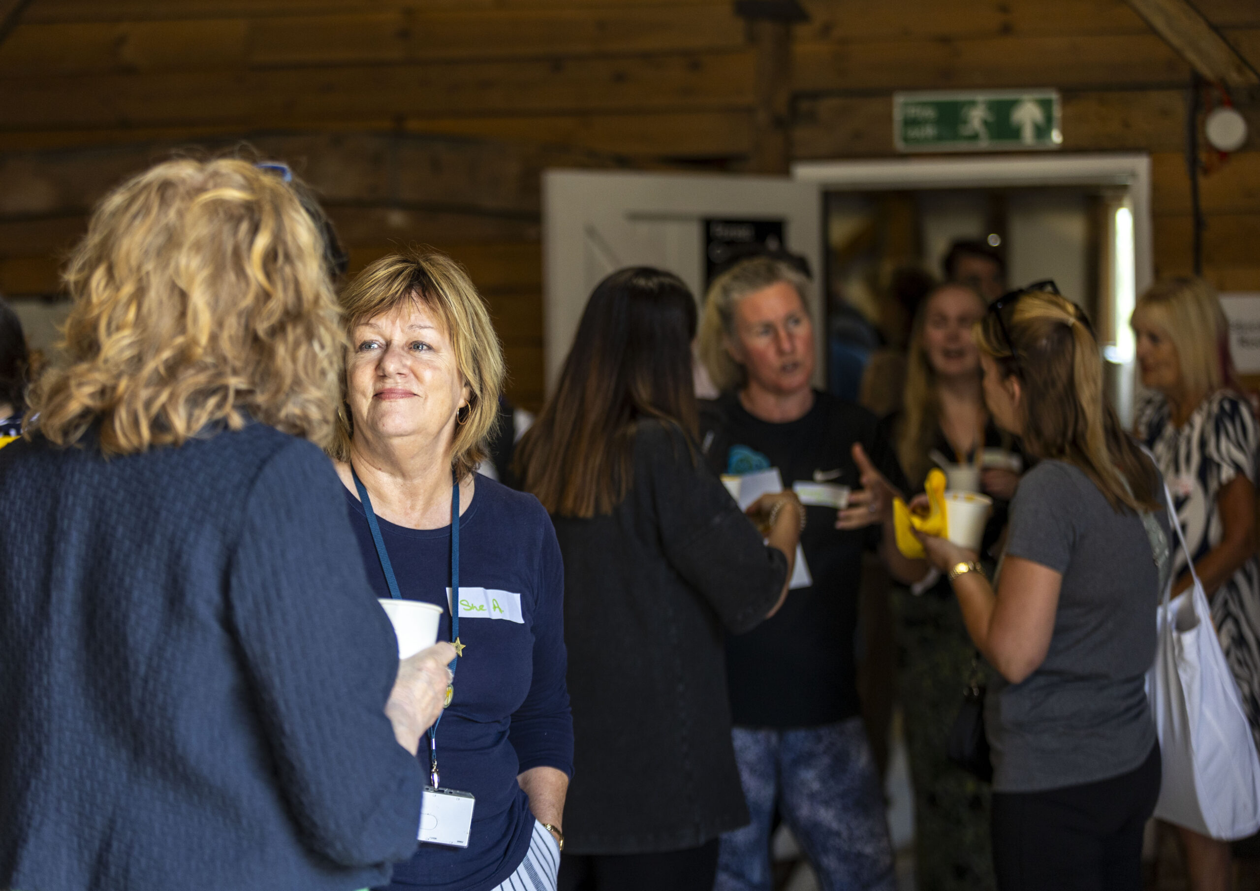 A group of people talking in a room with wooden walls; some hold cups, one holds a banana.