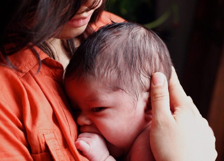 Person in an orange shirt gently cradling a baby with one hand