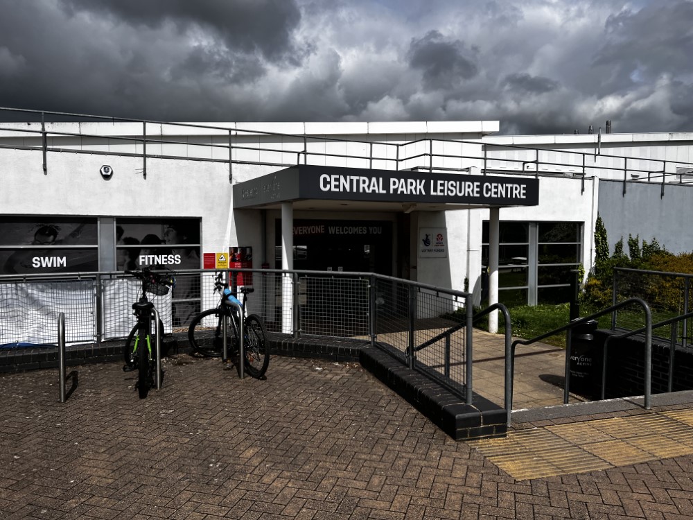 Central Park leisure centre Entrance to Central Park Leisure Centre with signage, parked bicycles, and window signs reading 'SWIM' and 'FITNESS' under a cloudy sky.