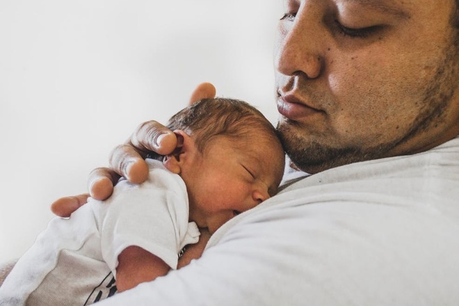 Adult holding a baby close, with the baby's head resting on their shoulder.