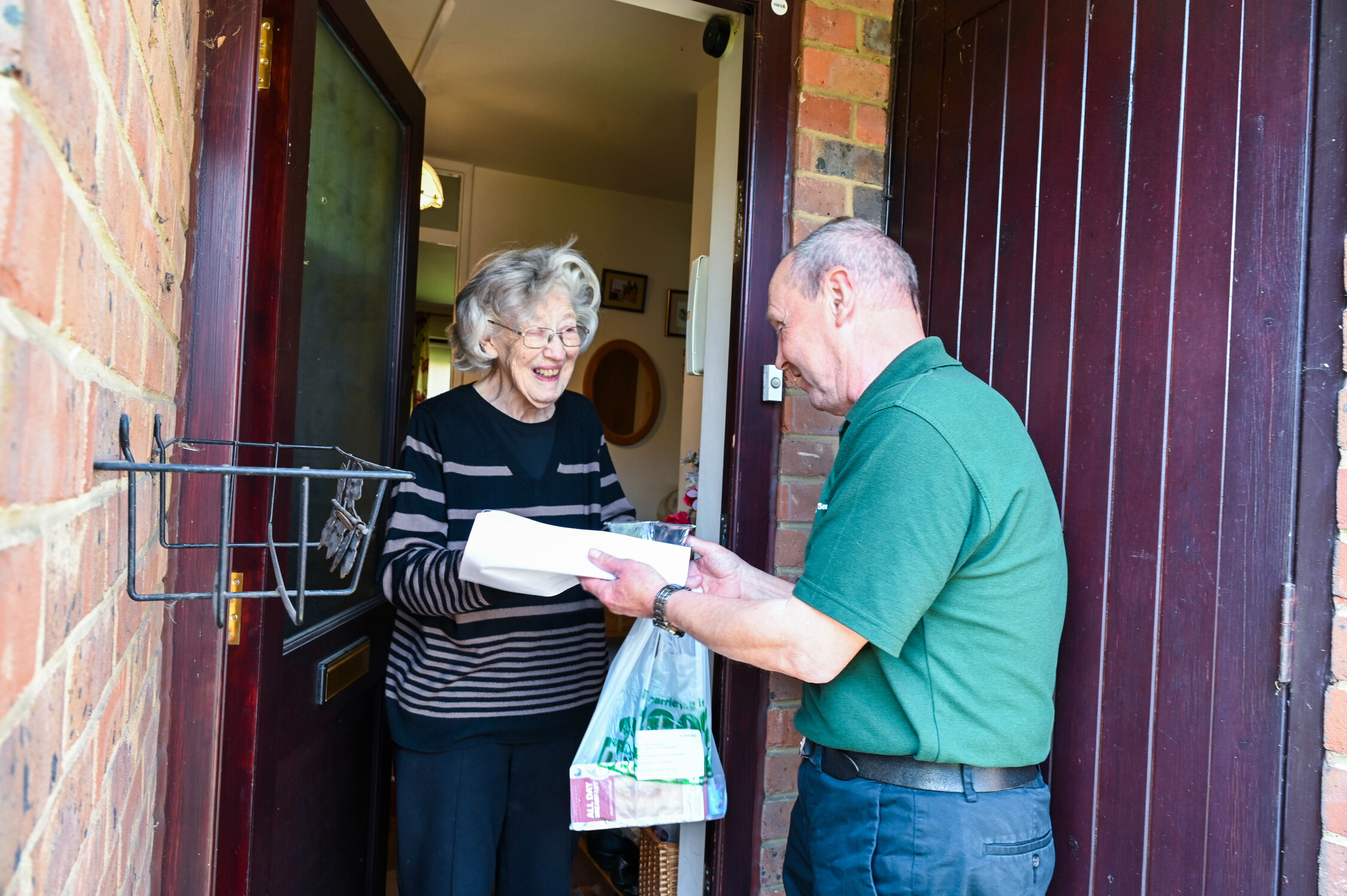 A man hands a food delivery to a lady at her doorstep