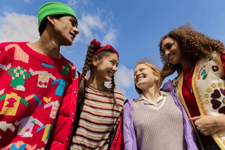 Four teenagers smiling in colour clothing stand outdoors under a blue sky.