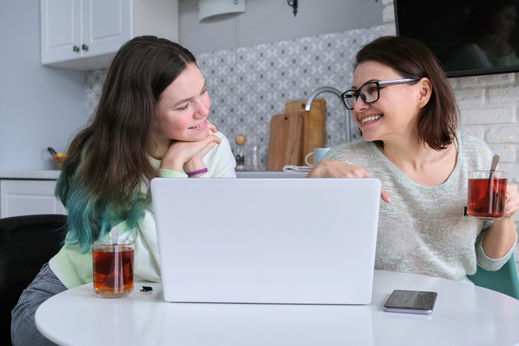 kitchen table Mother and teenage daughter sitting at the kitchen table in front of a laptop. They are smiling.