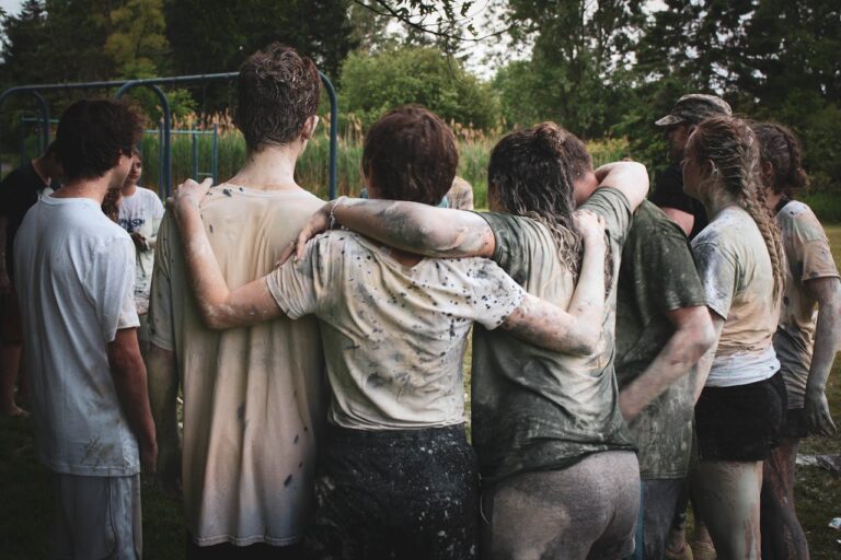 eight muddy team mates have their arms around each other with their backs to the camera.
