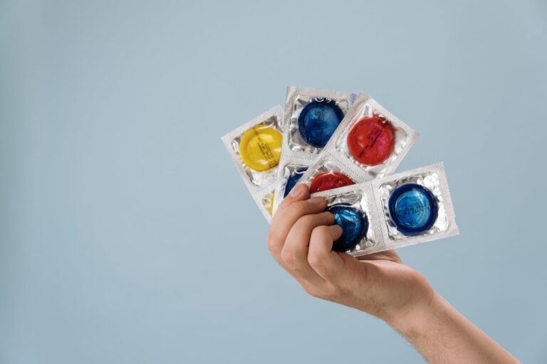 Someone holding 4 packets of condoms fanned out in their hands
