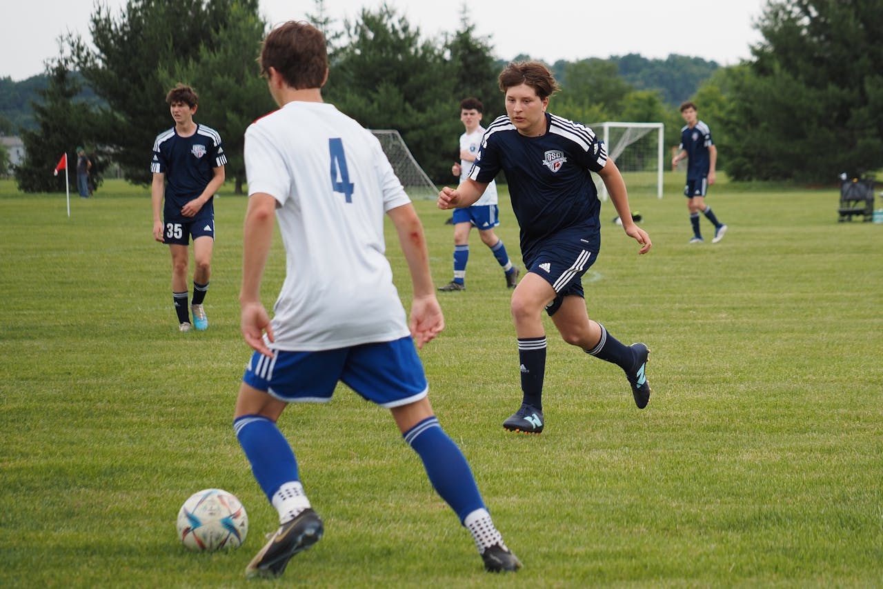 football A group of boys play football on a grassy floor. Player in a white Number 4 jersey prepares to kick the ball.
