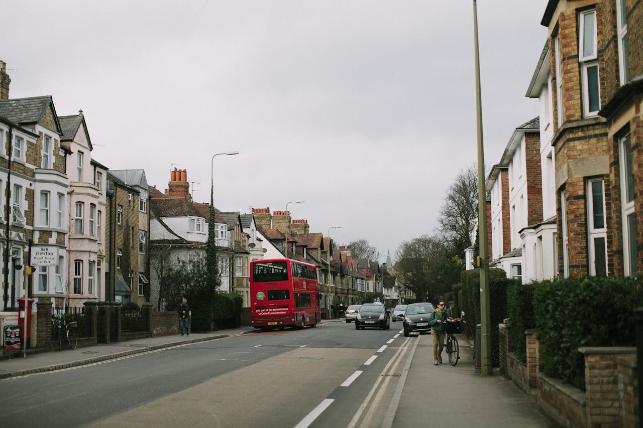 Photo of a street in the UK with houses along either side and a red London bus driving away from the camera