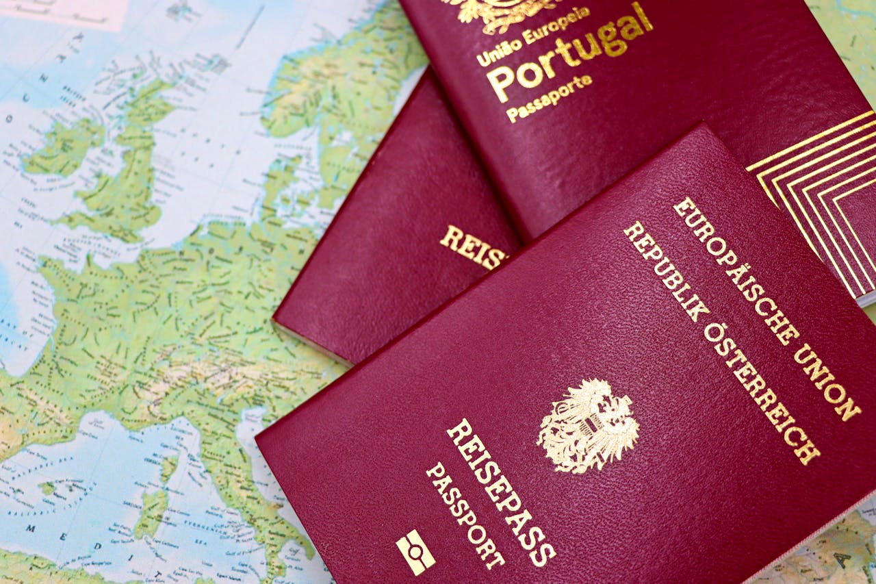 Three EU passports -two Austrian and one Portuguese-placed on a map of Europe, all burgundy with gold lettering and emblems.