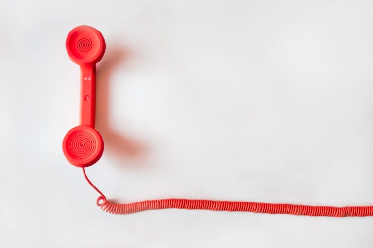 Red vintage telephone handset with coiled cord on a white surface.
