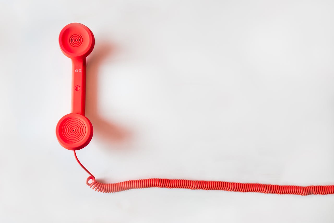 Red vintage telephone handset with coiled cord on a white surface.