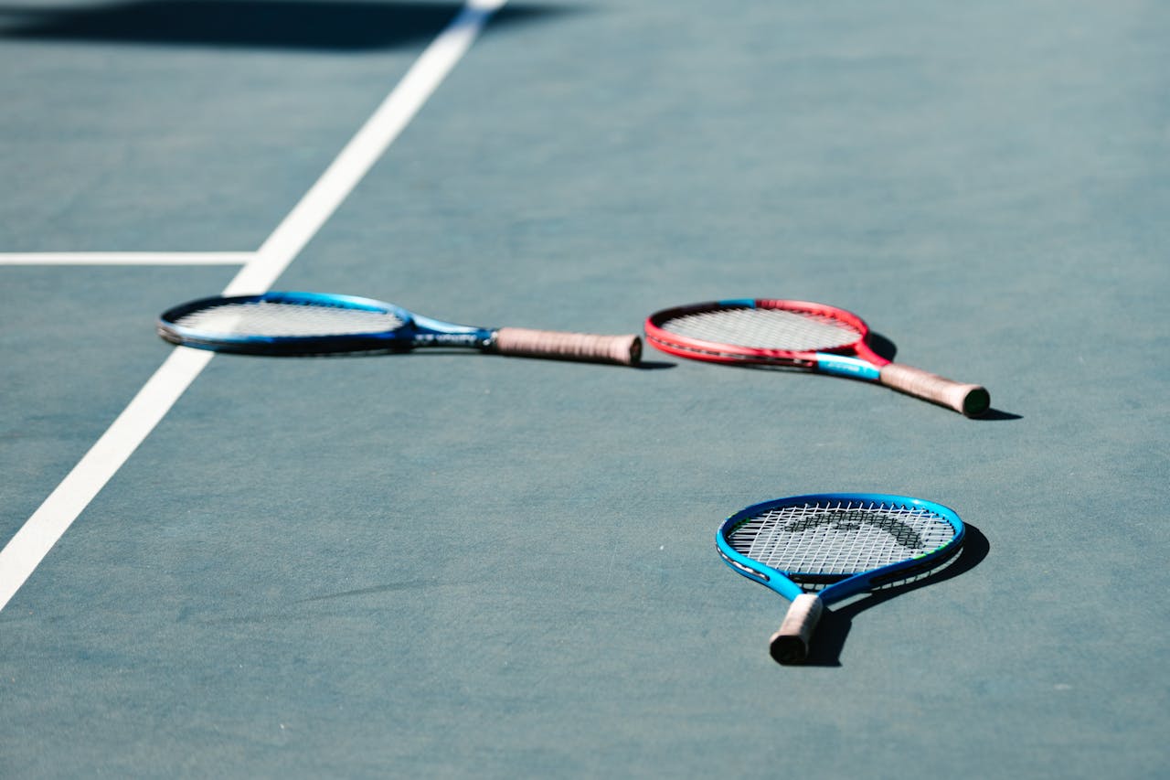 tennis raquets Three tennis rackets-two blue, one red-lying on a blue court with visible lines.