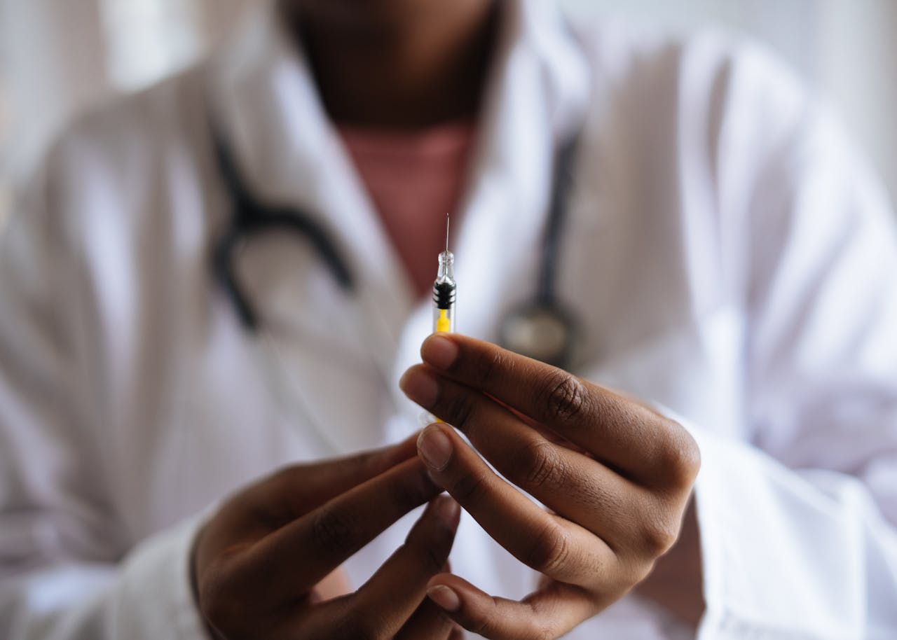 Person in a lab coat holding a syringe with yellow liquid.