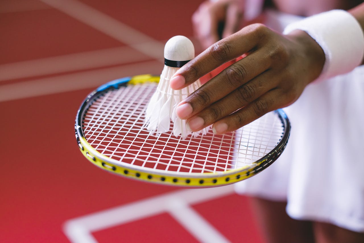 Close-up of a person holding a badminton racket and placing a shuttlecock on its strings, on an indoor court.