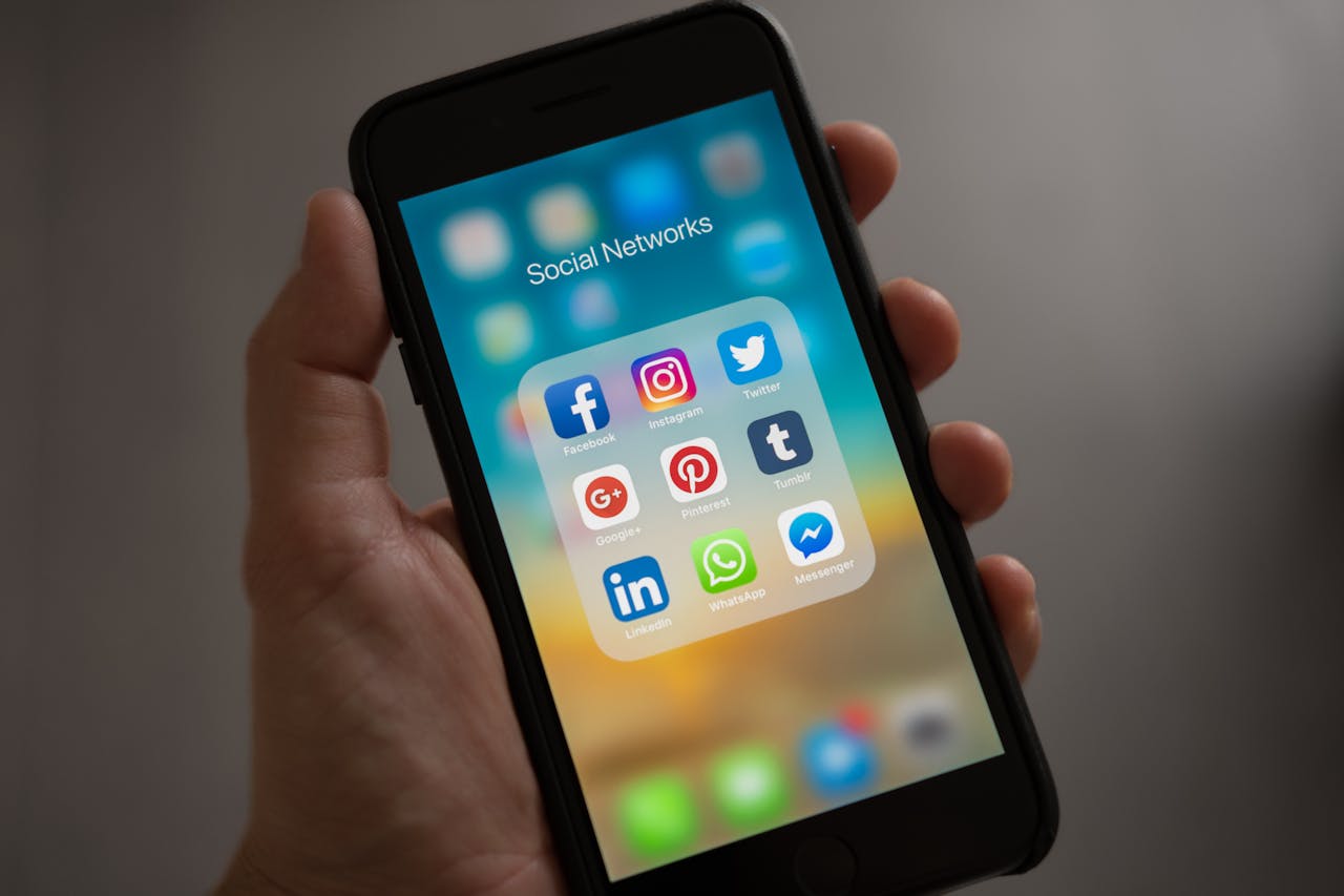 Hand holding a smartphone showing a folder labeled "Social Networks" with icons for popular social media apps.