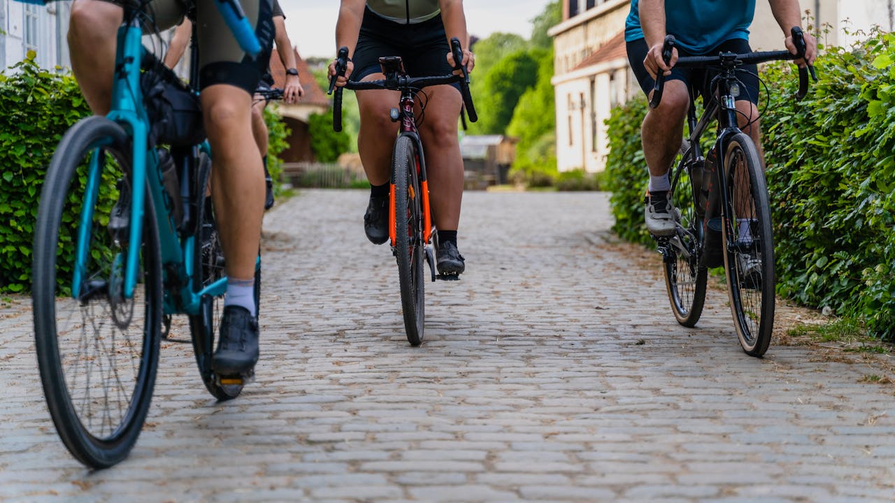 Cycle Three cyclists in a row, cycling down a bush-lined path.