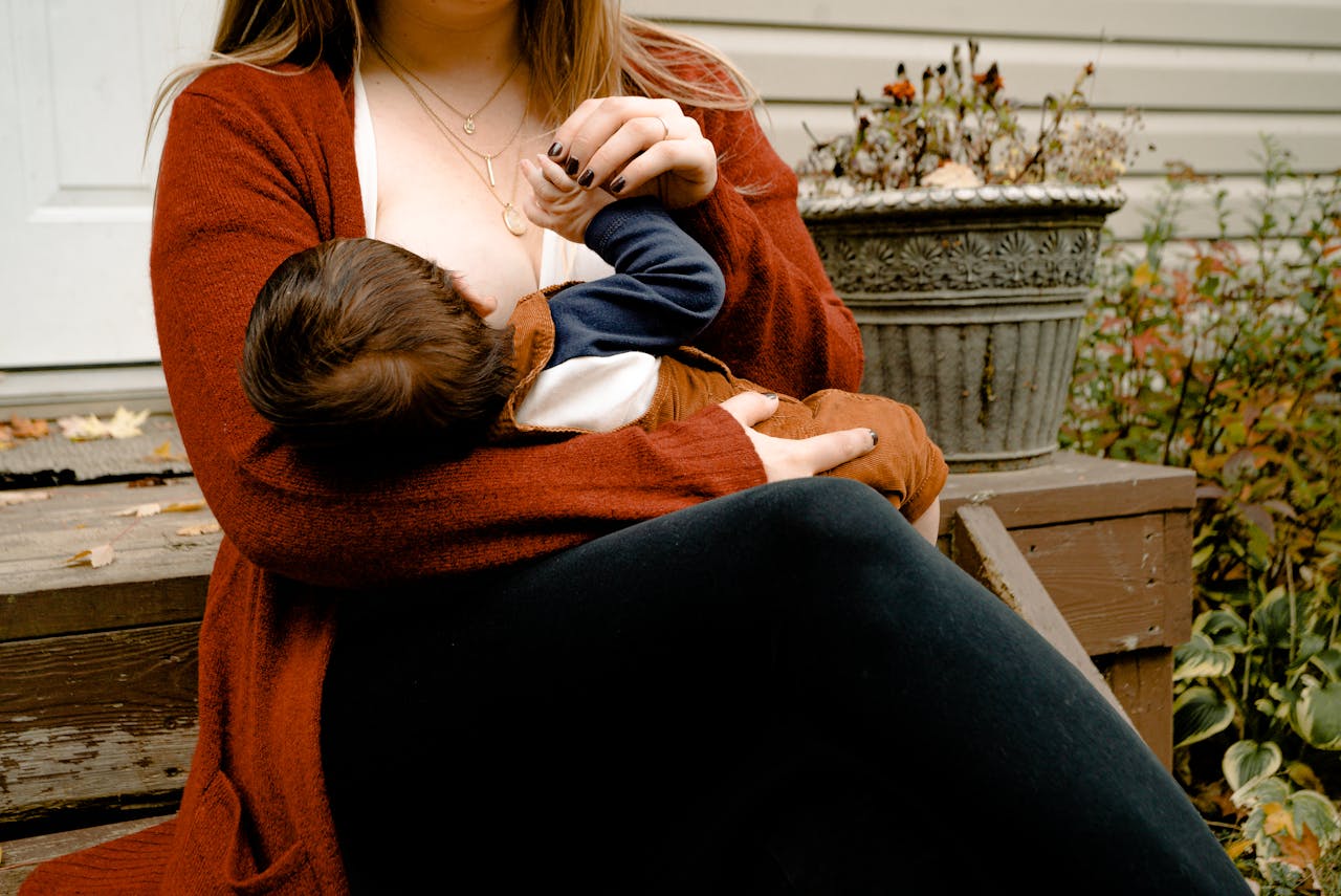 A lady wearing an orange cardigan breast feeds her baby whilst sat on a doorstep.