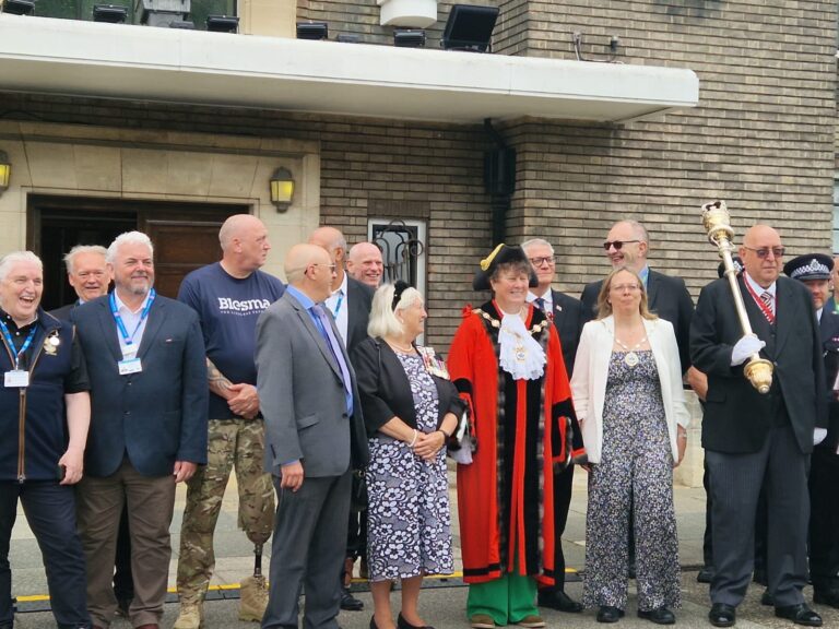 A group of people, including the mayor in a red ceremonial robe and chain, stand outside the Havering Town Hall building. Some wear formal attire, one person holds a ceremonial staff, and others wear badges or lanyards.