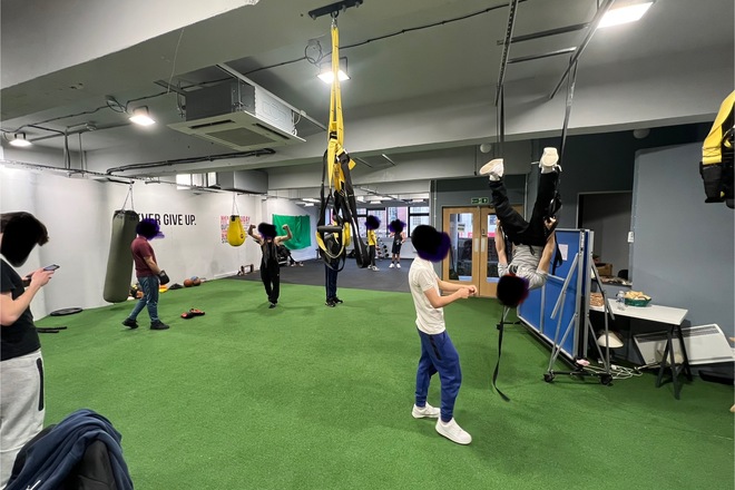 Teenagers are in an open space with boxing bags and other apparatus to support them to do physical activity.