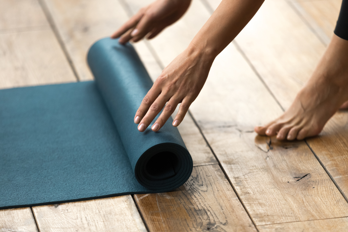 yoga mat A lady stands at the foot of a yoga mat, rolling it up.