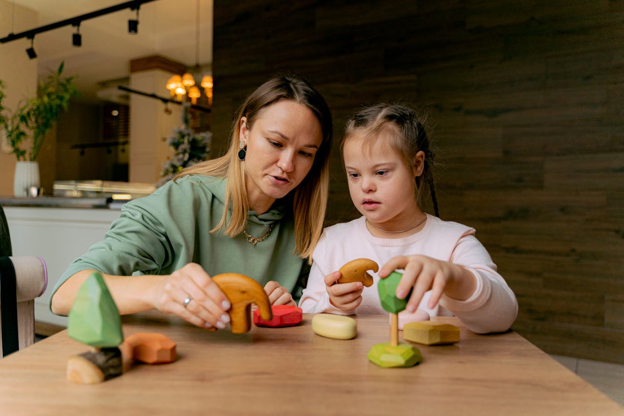 An adult and child sit at a wooden table playing with colourful wooden toys.