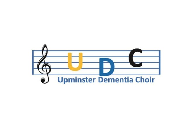 Logo for Upminster Dementia Choir showing a musical staff with a treble clef and the letters U (in yellow), D (in blue), and C (in black) above the words Upminster Dementia Choir.