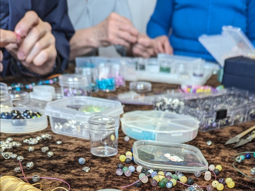 People sat together making bracelets with a wide array of beads and strong on a table.