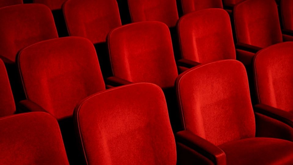Close up of red cinema chairs in a dark screening room.