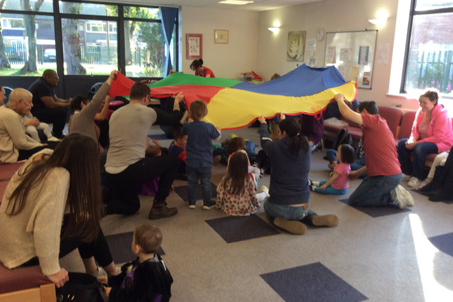 Children and their parent carers playing together in a hall with a parachute.
