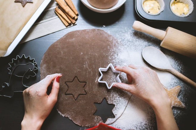 A person with red painted nails is using a star cookie cutter to cut out dark brown cookies.