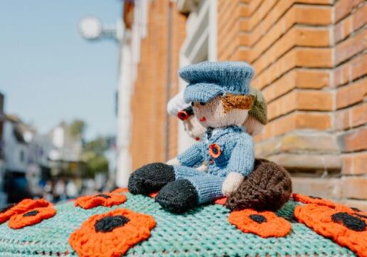 Two knitted figures in armed forces uniforms surrounded by poppies on top of a red postbox