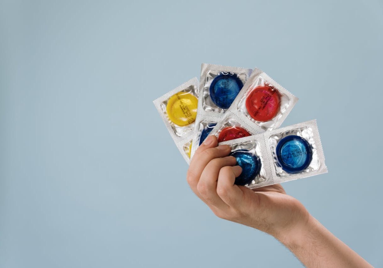 Someone holding 4 packets of condoms fanned out in their hands